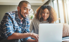 A young couple sitting on a couch and looking at a laptop together.