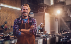 A man standing confidently in a workshop smiling at the camera.