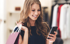 A young woman holding shopping bags and smiling while looking at her phone. 