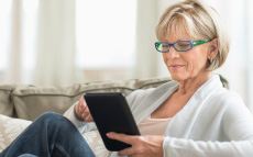 A senior woman casually lying on a couch using a tablet. 
